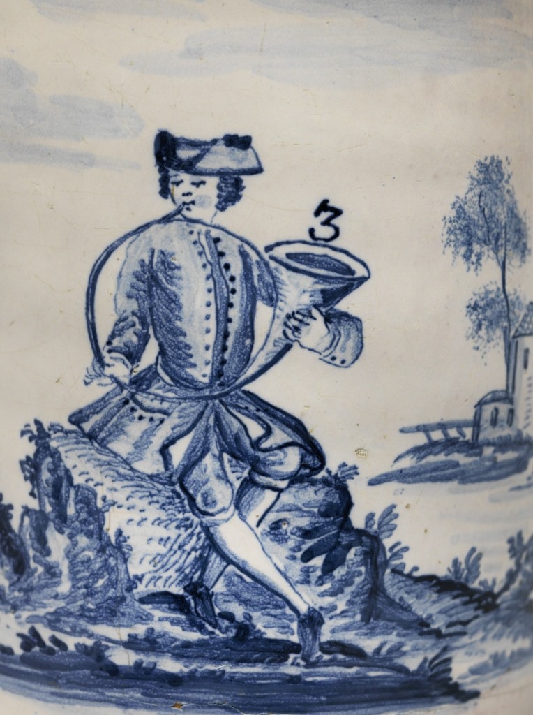 Nahaufnahme eines Fayencekrugs von 1758, abgebildet ist ein Mann, der in ein Horn bläst